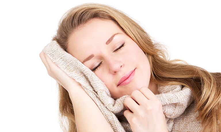 Una mujer con los ojos cerrados se pone un suéter en la cara.