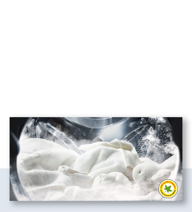 Una manta blanca suave y un peluche se muestran rociados con vapor en la tina de la lavadora.
