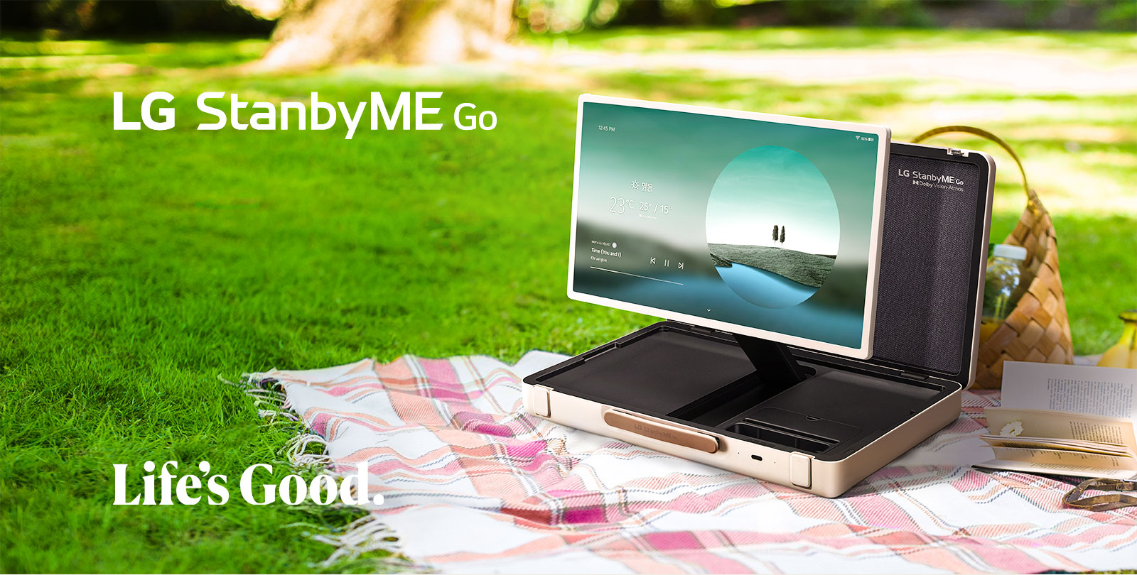 LG StanbyME Go se coloca sobre una manta de picnic a cuadros con el lado izquierdo hacia adelante y muestra una pantalla de inicio con el tema meteorológico.