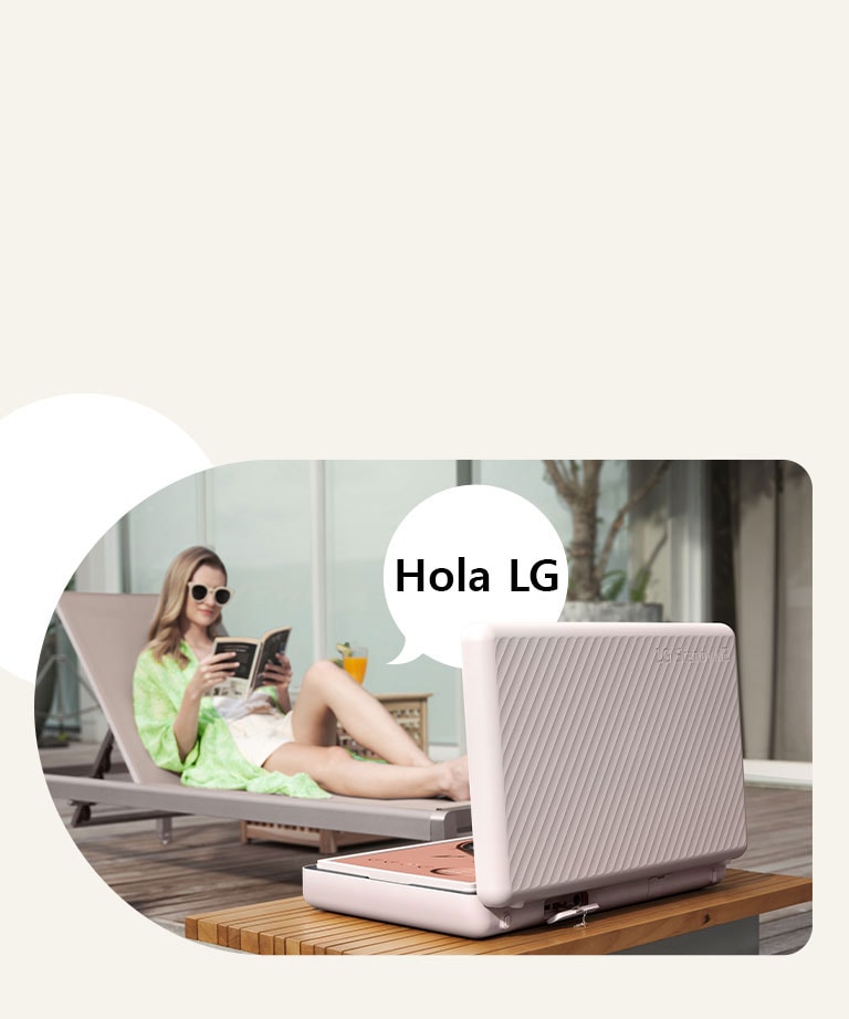 Vista trasera del LG StanbyME Go, y está colocado justo en frente de la mesa del patio. Una mujer se relaja en la silla de playa, controla la pantalla con su voz. Para ilustrar esto, se muestra una burbuja de diálogo con el texto Hola, LG en el lado derecho de ella.