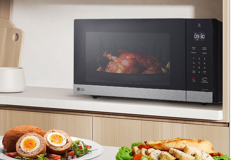 La imagen muestra una variedad de alimentos en la mesa de la cocina, y un pollo rostizado está siendo cocinado por el microondas NeoChef.