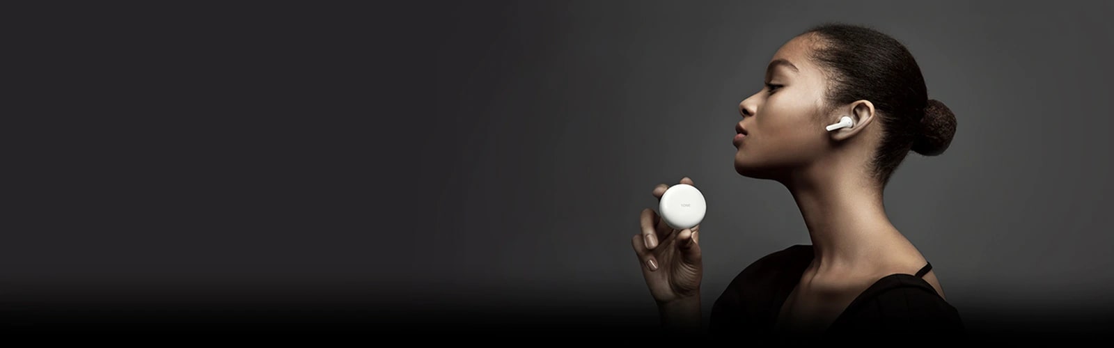 Vista lateral de una mujer sosteniendo TONE Free de LG contra un fondo oscuro.