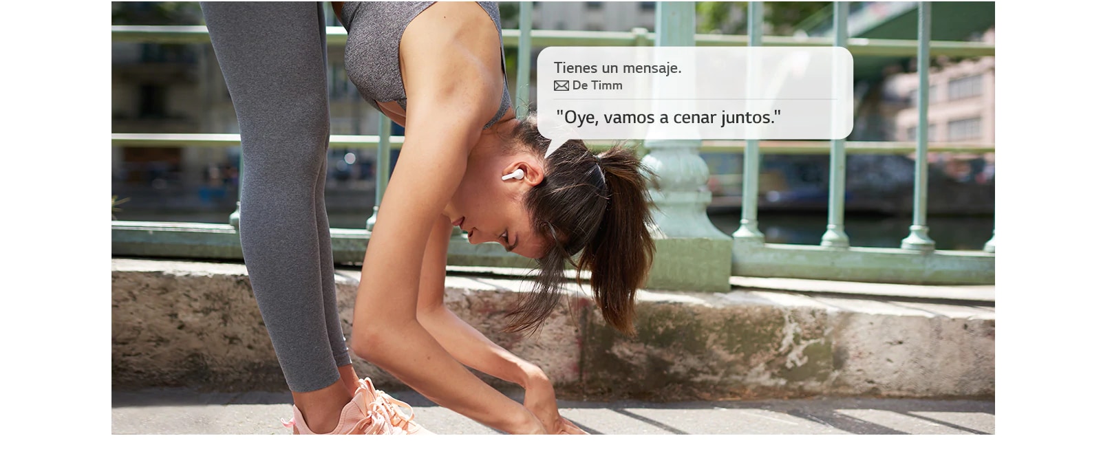 Una mujer se estira e inclina para tocar el suelo, mientras escucha un mensaje que le leen sus auriculares.