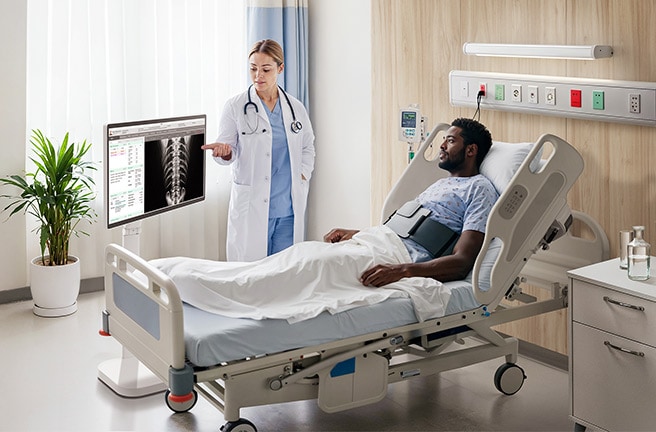 Un paciente está en una cama de hospital con dos médicos a su lado. Un LG Smart Monitor Swing está junto al médico.