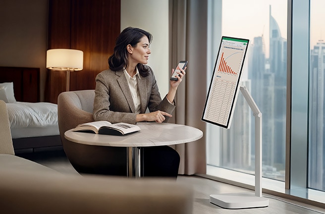 Una mujer está revisando un gráfico en un LG Smart Monitor Swing en una habitación de hotel.