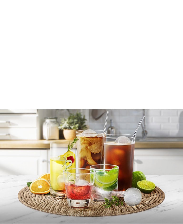 Varios vasos con diferentes bebidas y cubos de hielo redondos están sobre una encimera de cocina.