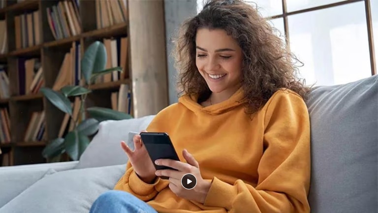 Mujer mirando su teléfono celular usando la aplicación LG Thinq para controlar su refrigerador LG de varias puertas de forma remota.