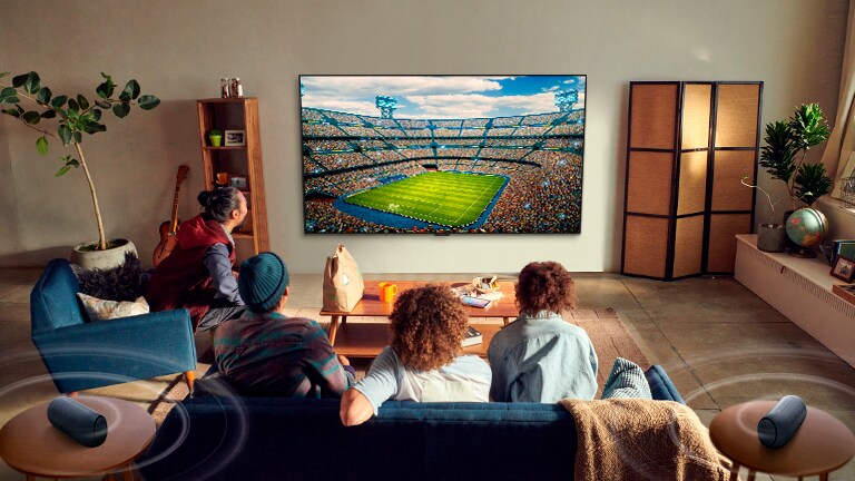Personas mirando un partido en la TV de la sala de estar con altavoces traseros Bluetooth