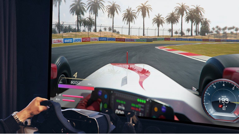 Primer plano de un jugador sosteniendo un volante mientras juega un juego de carreras en una pantalla de TV.