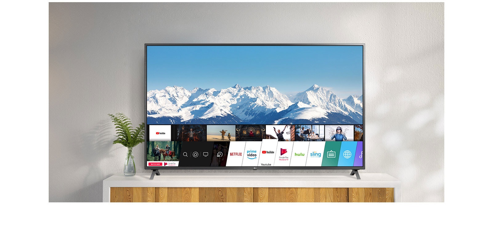 TV parada sobre un soporte blanco contra una pared blanca. La pantalla de TV muestra la pantalla de inicio con webOS.