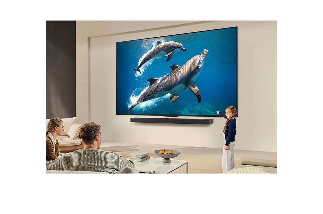 LG 86 pulgadas LG QNED AI QNED82 4K Smart TV 2025, A family sits on a couch facing a LG QNED TV mounted on a wall above a LG Soundbar with a little girl pointing to a screen depicting two dolphins. The title talks about how every action is more thrill, 86QNED82ASG, thumbnail 15