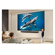 LG 86 pulgadas LG QNED AI QNED82 4K Smart TV 2025, A family sits on a couch facing a LG QNED TV mounted on a wall above a LG Soundbar with a little girl pointing to a screen depicting two dolphins. The title talks about how every action is more thrill, 86QNED82ASG, thumbnail 15