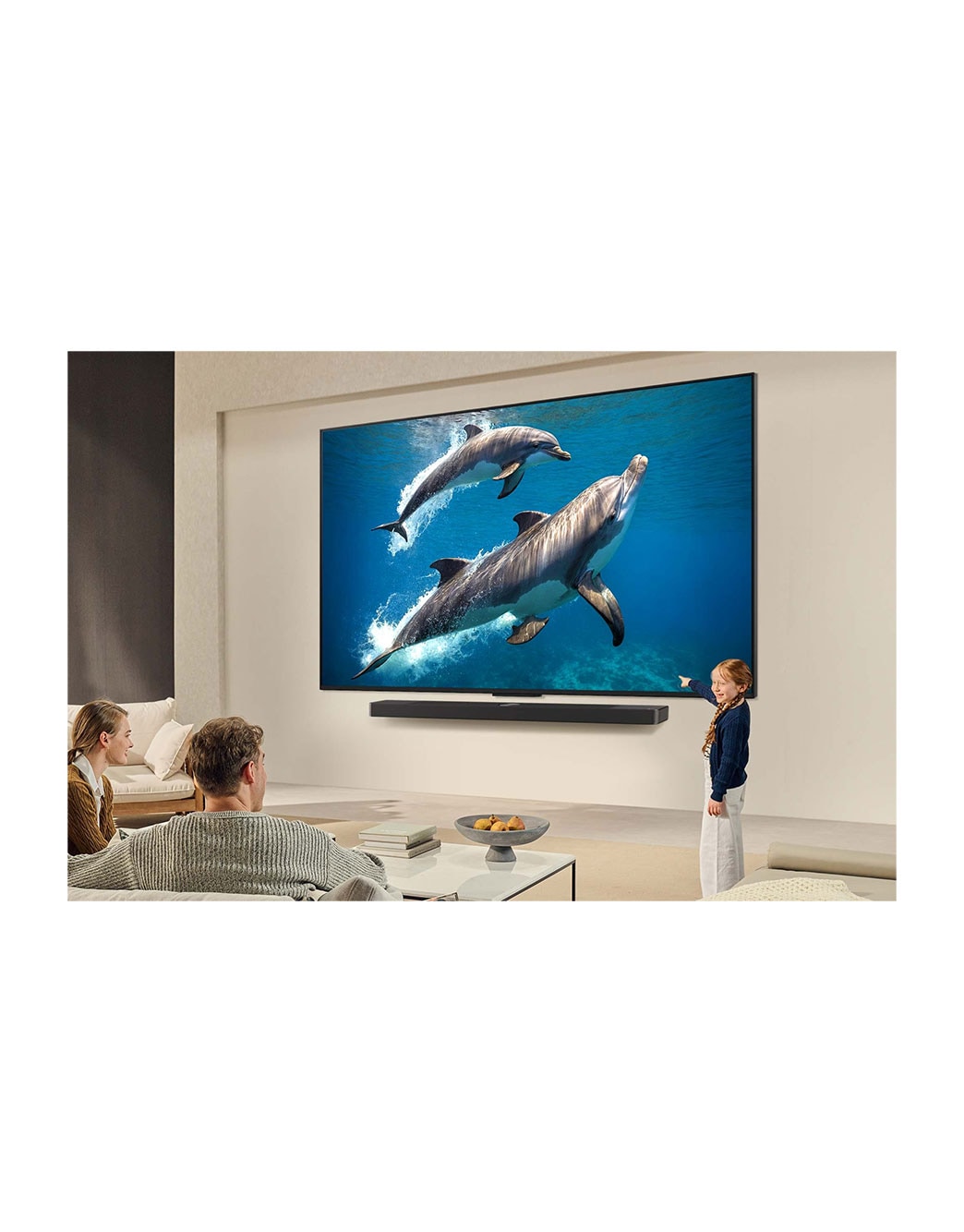 LG 43 pulgadas LG QNED AI QNED82 4K Smart TV 2025, Una familia sentada en el sillón frente a la LG QNED TV montada en la pared encima de una LG Soundbar; una pequeña niña señala la pantalla que muestra dos delfines. El título habla de cómo las escenas, 43QNED82ASG, thumbnail 14