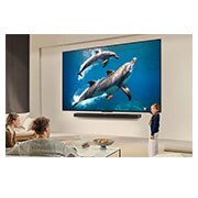 LG Pantalla 55 pulgadas LG QNED AI QNED70 4K SMART TV 2025, A family sits on a couch facing a LG QNED TV mounted on a wall above a LG Soundbar with a little girl pointing to a screen depicting two dolphins. The title talks about how every action is more thrill, 55QNED70ASA, thumbnail 14