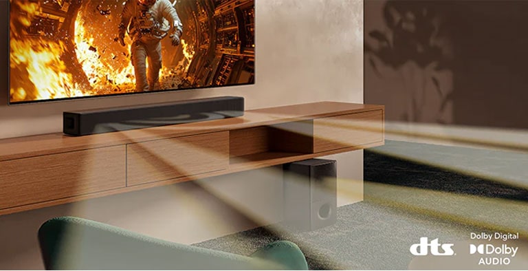 Se muestra un televisor con contenido científico y la barra de sonido SH5A se encuentra justo debajo. En el piso también se encuentra el subwoofer de la barra de sonido. De la barra de sonido y del subwoofer salen ondas sonoras blancas semitransparentes. En la parte inferior derecha se encuentran los logotipos de DTS y Dolby Digital Audio.