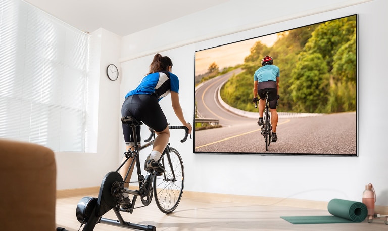 Una mujer trabaja virtualmente con una laptop y un tv grande colgado en la pared en la sala de estar.