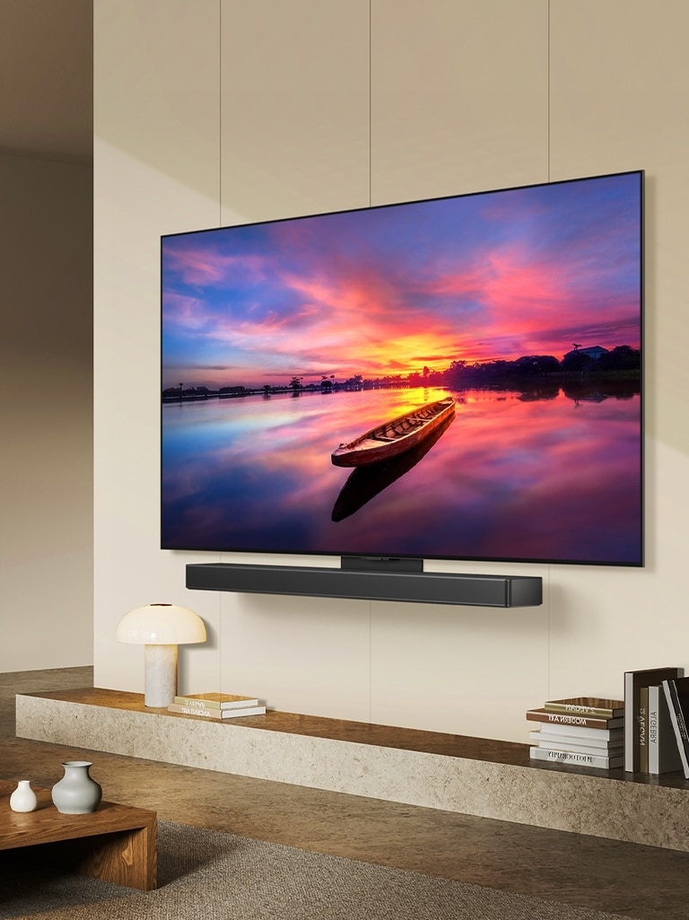 Der LG OLED evo TV C4, 45 Grad nach links geneigt, zeigt einen wunderschönen Sonnenuntergang mit einem Boot auf einem See. Der Fernseher ist über das Matching-Kit an einer LG Soundbar in einem minimalistischen Wohnraum befestigt.