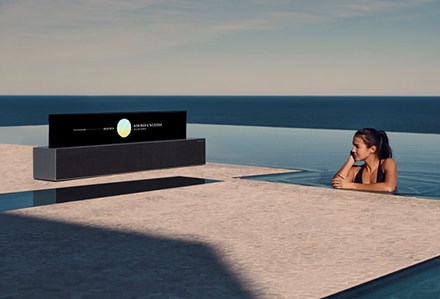 Une femme dans une piscine écoute une télévision OLED TV R enroulable en mode Affichage en ligne.
