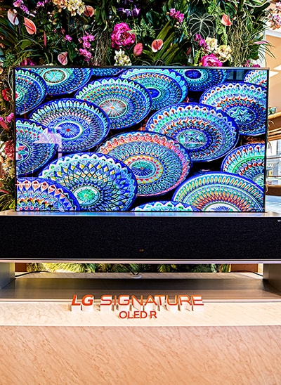 Télévision OLED R enroulable installée devant un mur de fleurs lors d'un événement célébrant la collaboration entre LG et BVLGARI.