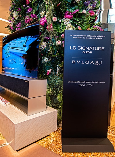Un support avec les noms LG SIGNATURE et BVLGARI situé à côté d'une télévision OLED R enroulable.
