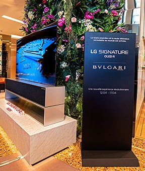 Un support avec les noms LG SIGNATURE et BVLGARI situé à côté d'une télévision OLED R enroulable.
