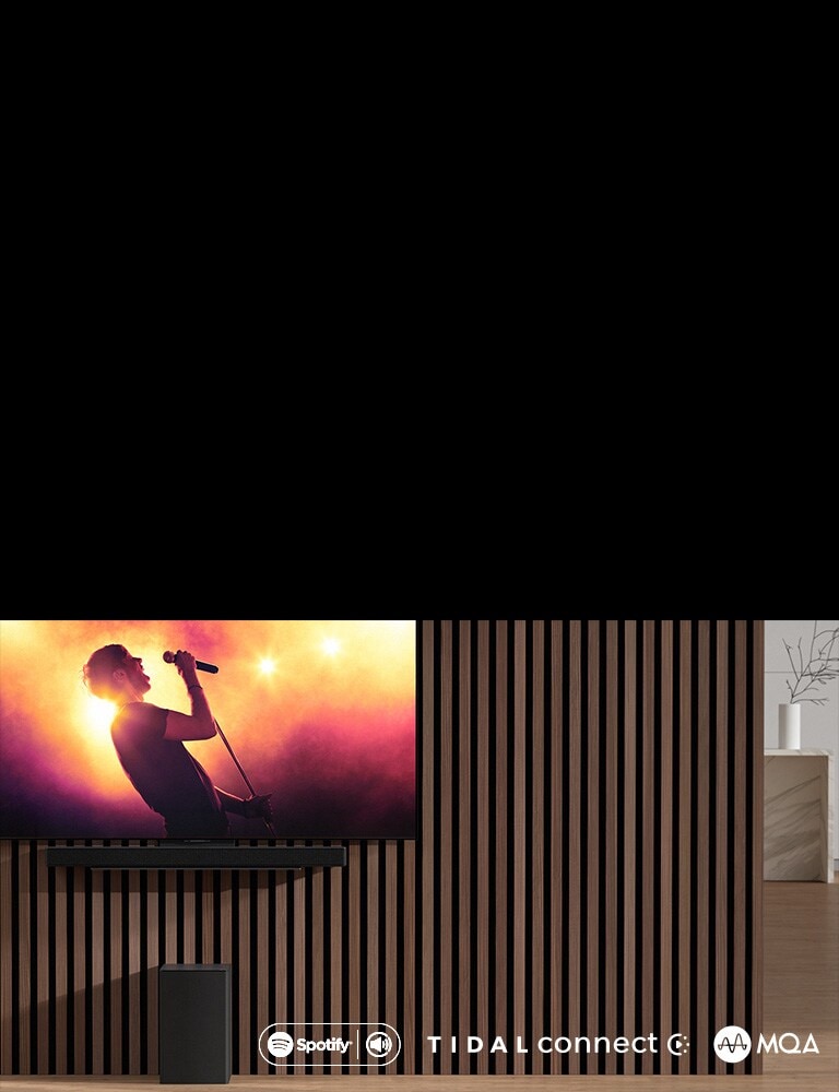 LG OLED C 挂在墙壁上，下方使用专用支架放置 LG 无线环绕回音壁 SC9S。音箱底下放置着超低音音箱。电视正播放音乐会的场景。