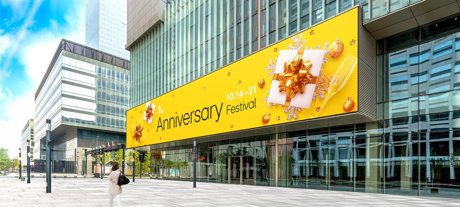A large LED screen is installed on the exterior wall of the building entrance, and a woman is watching the advertisements on its screen. The screen remains clear and visible despite the bright sunlight.	