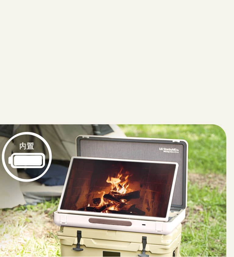 The LG StanbyME Go is placed in front of a tent, and the screen displays one of the relaxing themes--a fireplace. On the left top corner, built-in battery icon is shown.