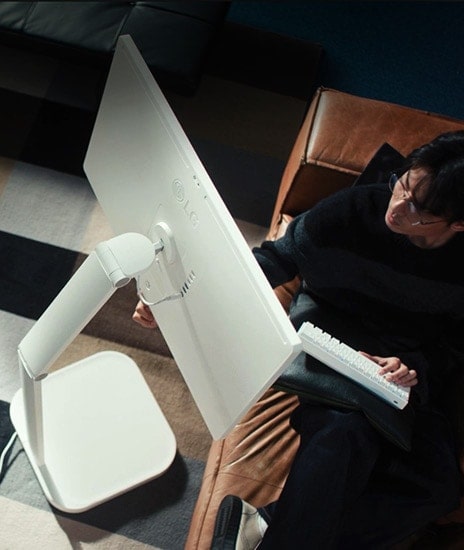 A man is holding a keyboard in one hand while touching the screen of a LG Smart Monitor Swing with the other.	