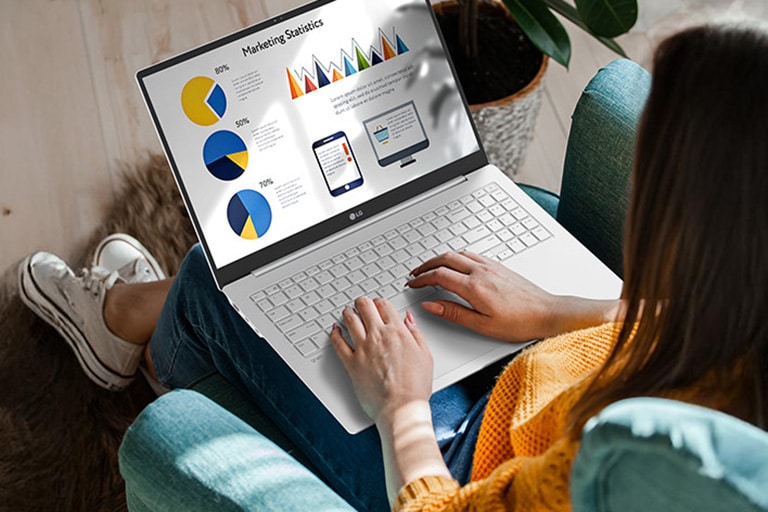 A person sitting comfortably in a chair, using a laptop that displays a presentation with charts and graphs. An animation demonstrates the anti-glare screen by showing no light reflection even when sunlight shines directly onto the display.	