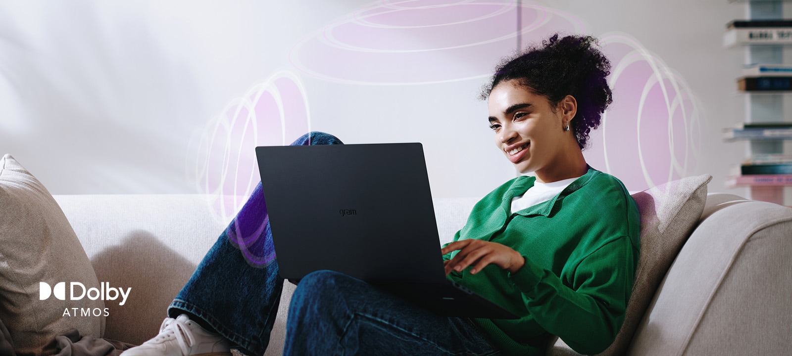 A person sitting on a couch, enjoying immersive audio while using an LG gram laptop. The text highlights Dolby Atmos technology, emphasizing a rich, expansive, 360-degree auditory experience. Surrounding sound waves in the background visually represent the immersive soundscape.	