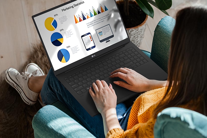 A person sitting comfortably in a chair, using a laptop that displays a presentation with charts and graphs. An animation demonstrates the anti-glare screen by showing no light reflection even when sunlight shines directly onto the display.