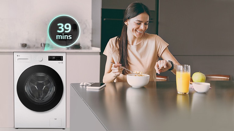 女士坐在桌旁看着手表，身后有一台洗衣机