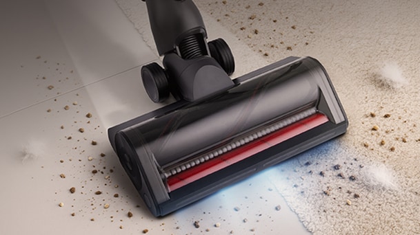 LG black vacuum cleaner powered floor head shows a red brush roller and blue light while it cleans debris near the carpet.