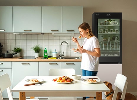 Geladeira LG de 2 portas rosa e preta em uma cozinha moderna. Uma mulher toma café da manhã em uma mesa com comida.