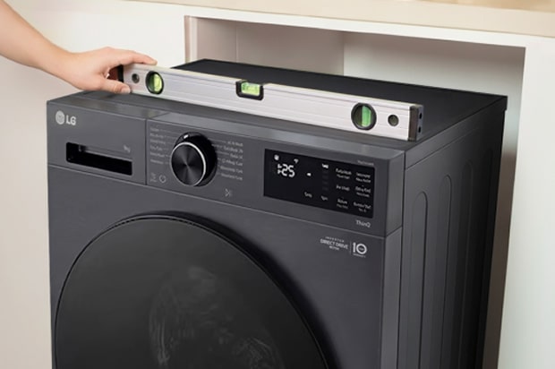 Lavadora de roupas LG preta com um nível de bolha colocado em cima para verificar se o aparelho está alinhado horizontalmente.	