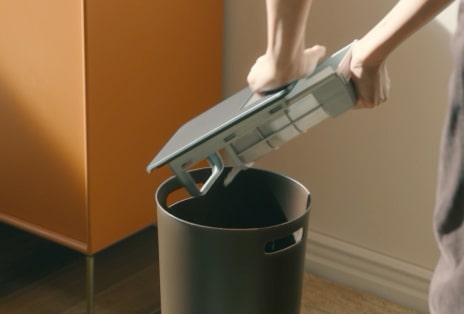 Mulher descartando fiapos de um filtro de secadora enquanto a limpeza automática do condensador é indicada na tela.