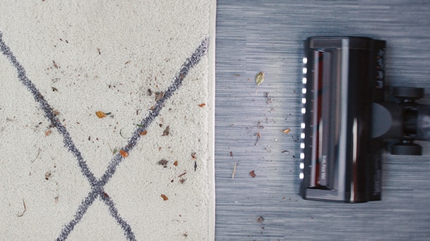 LG CordZero® Q3 Cordless Stick Vacuum in graphite powered floor head shows a red brush roller and light while it cleans debris near the carpet.