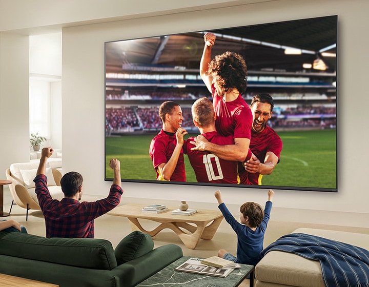 LG QNED evo AI Mini LED QNED8M Ultra Big TV shows an intense, large-scale soccer play with refined picture quality and vivid colors as a family cheers together from sofas in a living room.