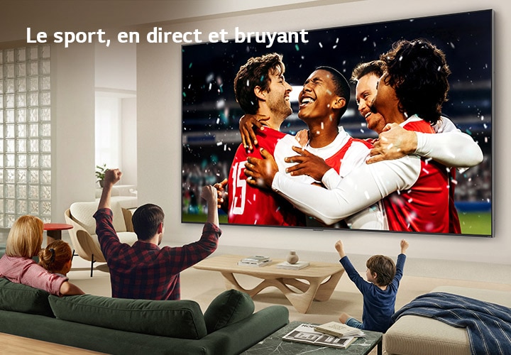 Un téléviseur LG Ultra Big fixé au mur dans un salon lumineux montre une célébration sportive dans un stade aux couleurs vives et à une qualité d’image raffinée sur un grand écran, tandis qu’une famille assise sur des sofas acclame ensemble.