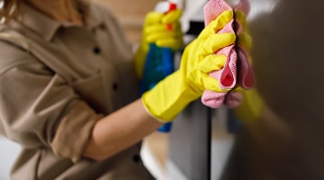 Persona con guantes amarillos limpia el exterior de un refrigerador LG con paño rosa, dejando la superficie impecable y lustrosa.