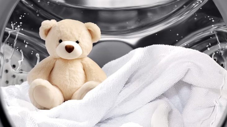 Tambor de lavadora LG de carga frontal con un osito de peluche de color beige claro y toallas blancas en su interior
