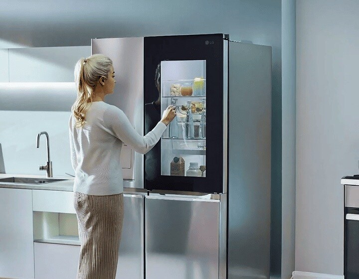 Una mujer da dos golpes en el refrigerador LG InstaView. El panel de cristal se ilumina para mostrar las botellas de agua que hay en su interior. Después abre la puerta y saca una.