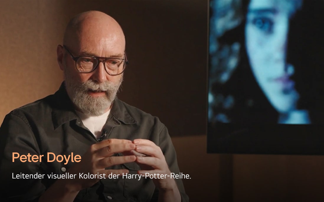 Peter Doyle, der leitende Kolorist der Harry-Potter-Reihe, spricht in einer warmen, sanft beleuchteten Umgebung. Er untermalt seine Worte mit Gesten, wodurch seine professionelle und nachdenkliche Atmosphäre entsteht.