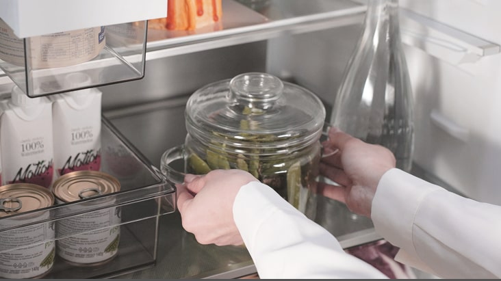 Person placing a glass jar of pickles inside LG refrigerator, showing organized storage.	