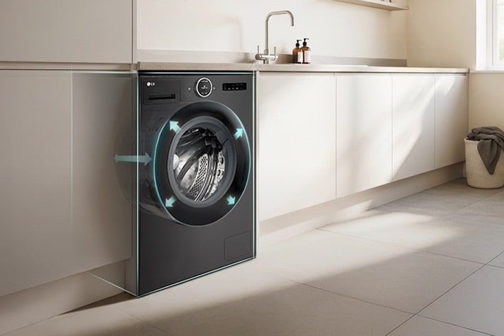 LG front load washing machine built into kitchen cabinetry. Arrows point outward from the drum to indicate size. A modern living room is visible next to the kitchen.