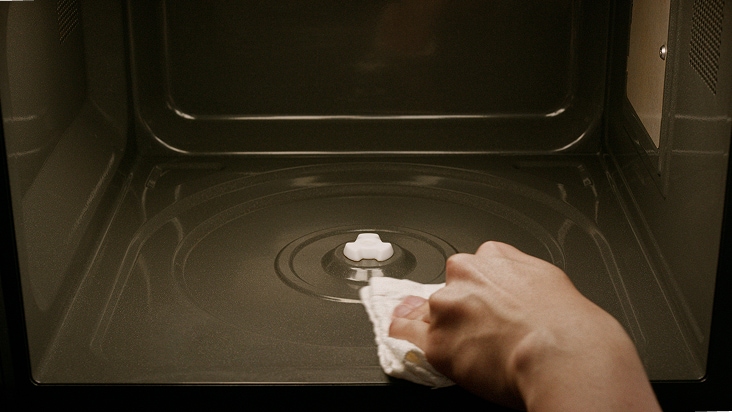 A hand wipes the black microwave interior using a white cloth.