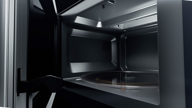 A microwave door stands open, showing a black interior with a round glass turntable and a metallic ceiling.