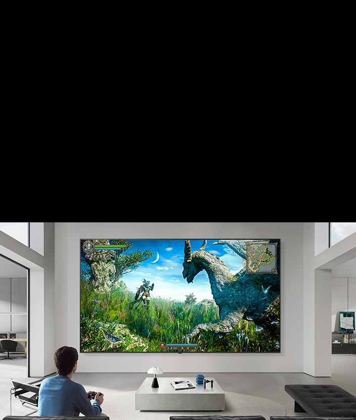 LG TV appears mounted on a wall in a black-and-white-toned living room, showing a fantasy dinosaur game scene on a large display while a person sits on a sofa holding a controller.