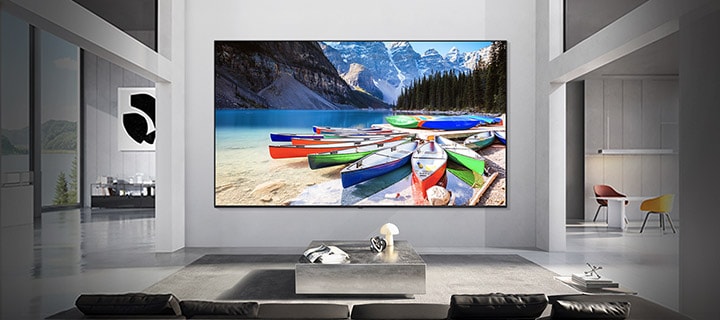 LG TV is wall-mounted in a modern living space, where a display shows a vivid lakeside scene with colorful boats and mountains, illustrating how screen size fits the space for a balanced and immersive viewing experience.